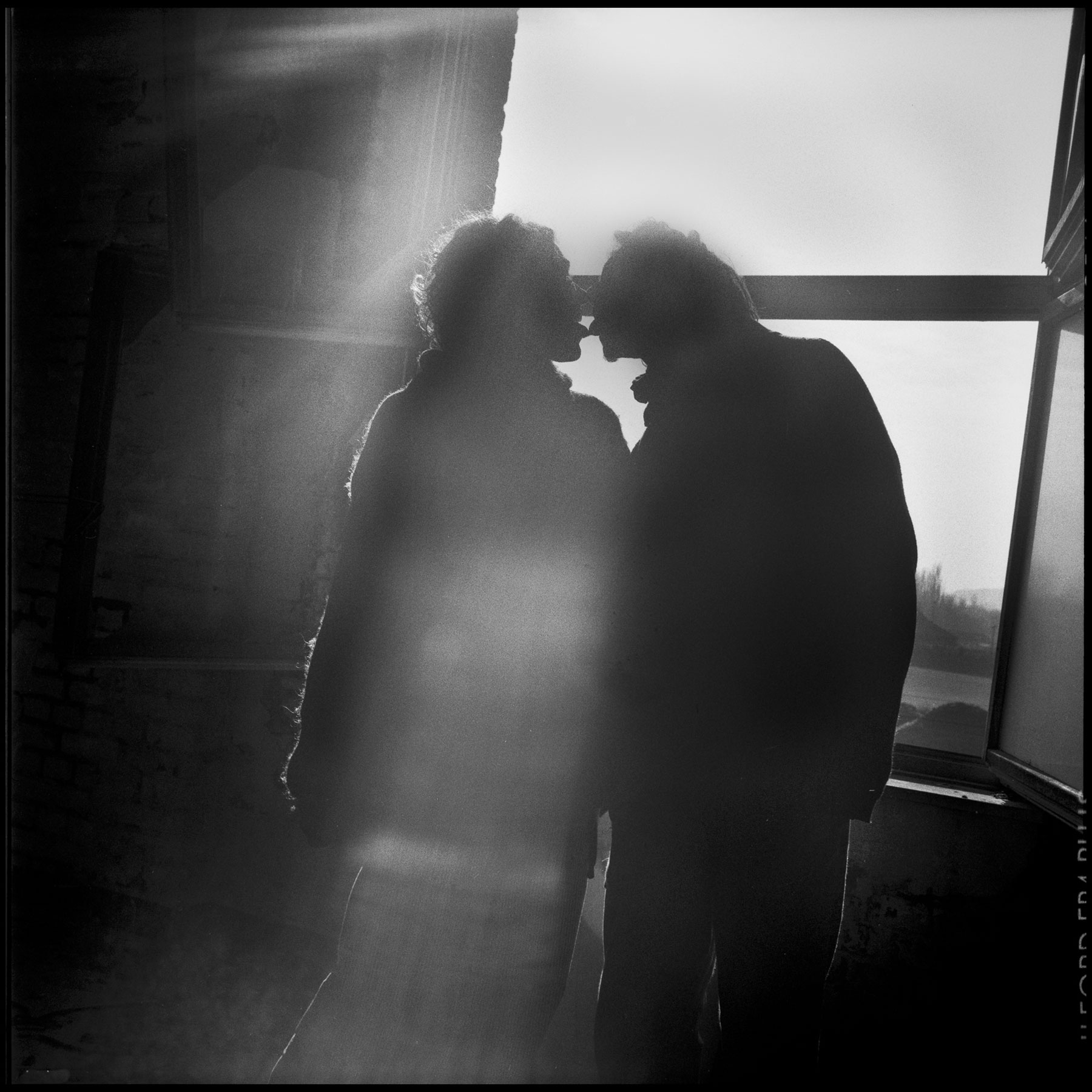 un-couple-en-contre-jour-s'embrasse-devant-une-fenêtre
