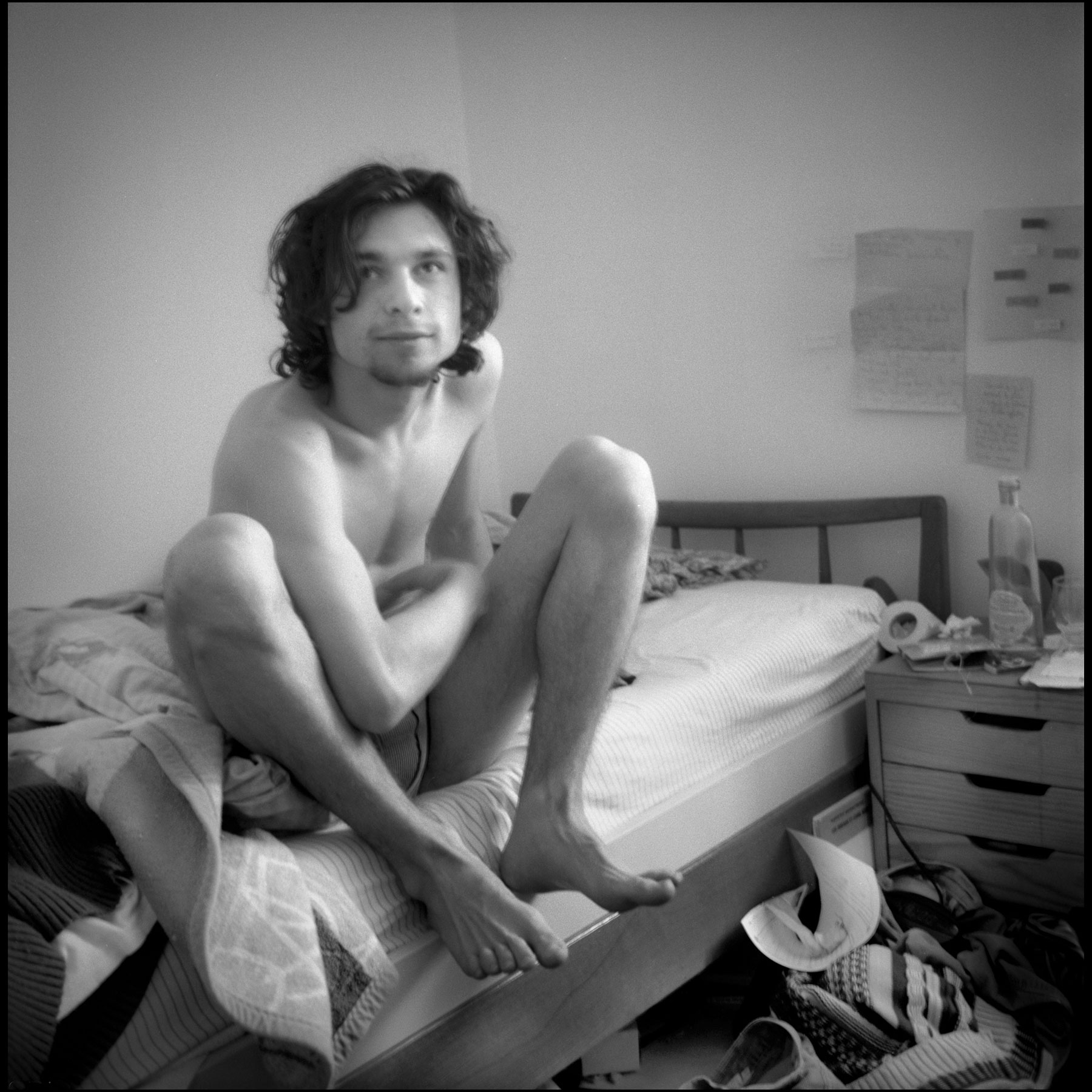 jeune-homme-cheveux-longs-bouc-assis-sur-lit-chambre-etudiante-noir-et-blanc